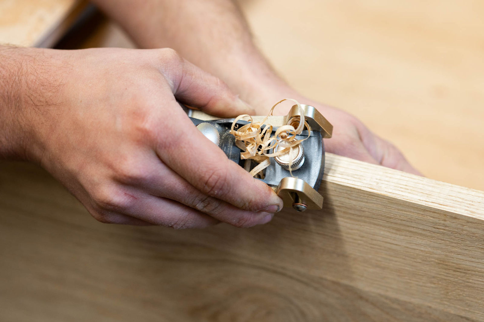Hände führen einen Handhobel über Holz